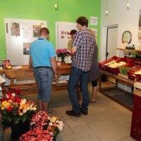 Kunden stehen im Hofladen und schauen sich frische Blumen und Produkte an