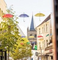 Bunte Regenschirme hängen über einer Einkaufsstraße in Ibbenbüren, im Hintergrund ist eine Kirche zu sehen