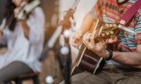 Ein Mann spielt Gitarre und im Hintergrund spielt eine Frau Geige Ein Mann spielt Gitarre und im Hintergrund spielt eine Frau Geige