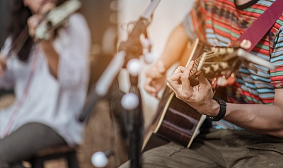 Mann spielt Gitarre und im Hintergrund spielt eine Frau Geige