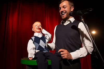Bauchredner mit Puppe auf der Bühne vor rotem Vorhang