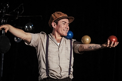 Das Bild zeigt einen Schauspieler mit Hut, der drei Bälle auf seinem Arm balanciert.